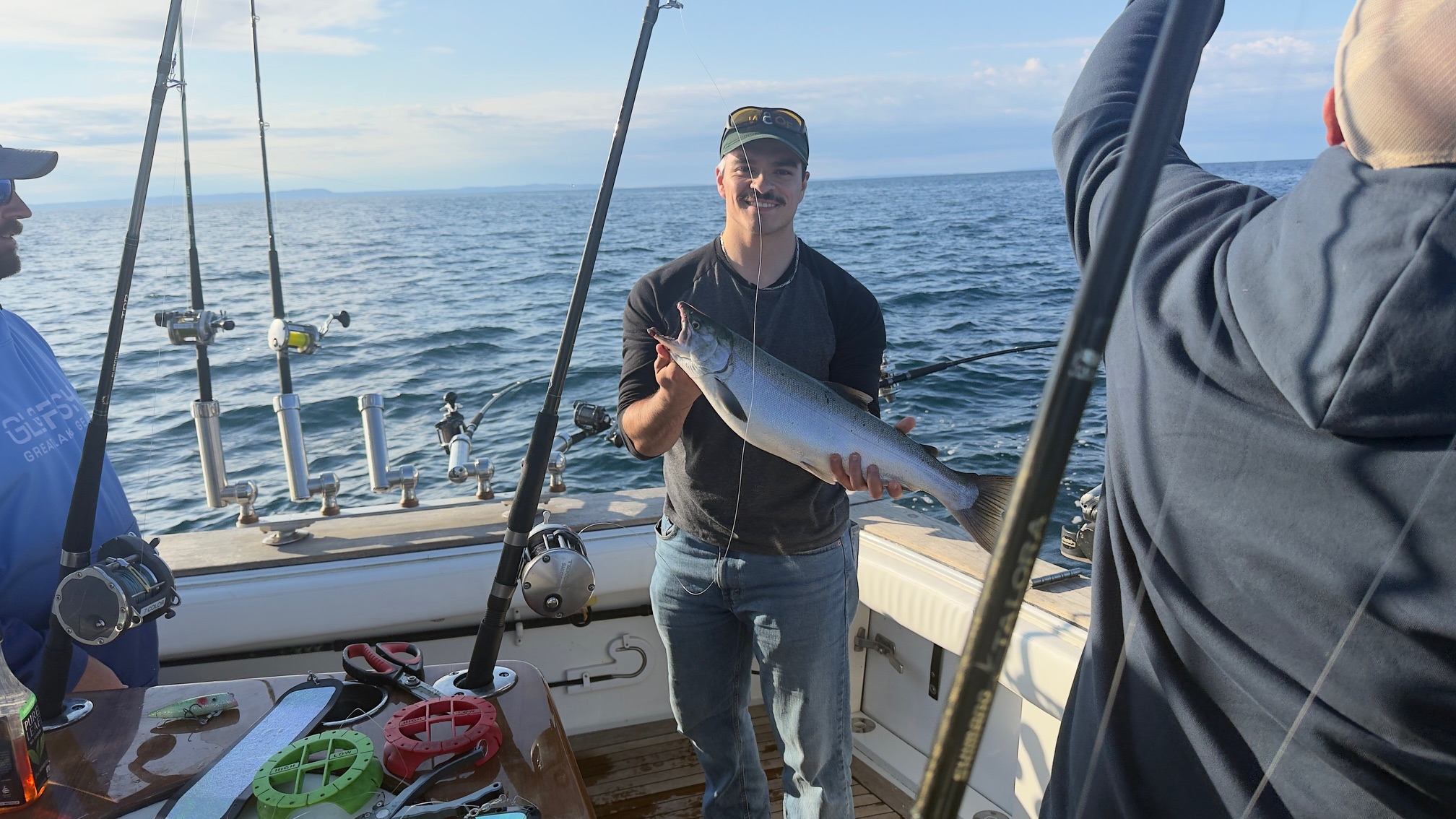 Anthony holding a salmon on a boat on Lake Michigan, rods in the holders, Frankfort trip August 28, 2026